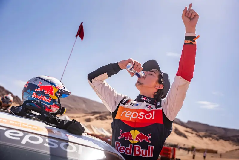 Seth Quintero celebrating with his arm raised beside his Toyota Hilux at the Rally of Morocco
