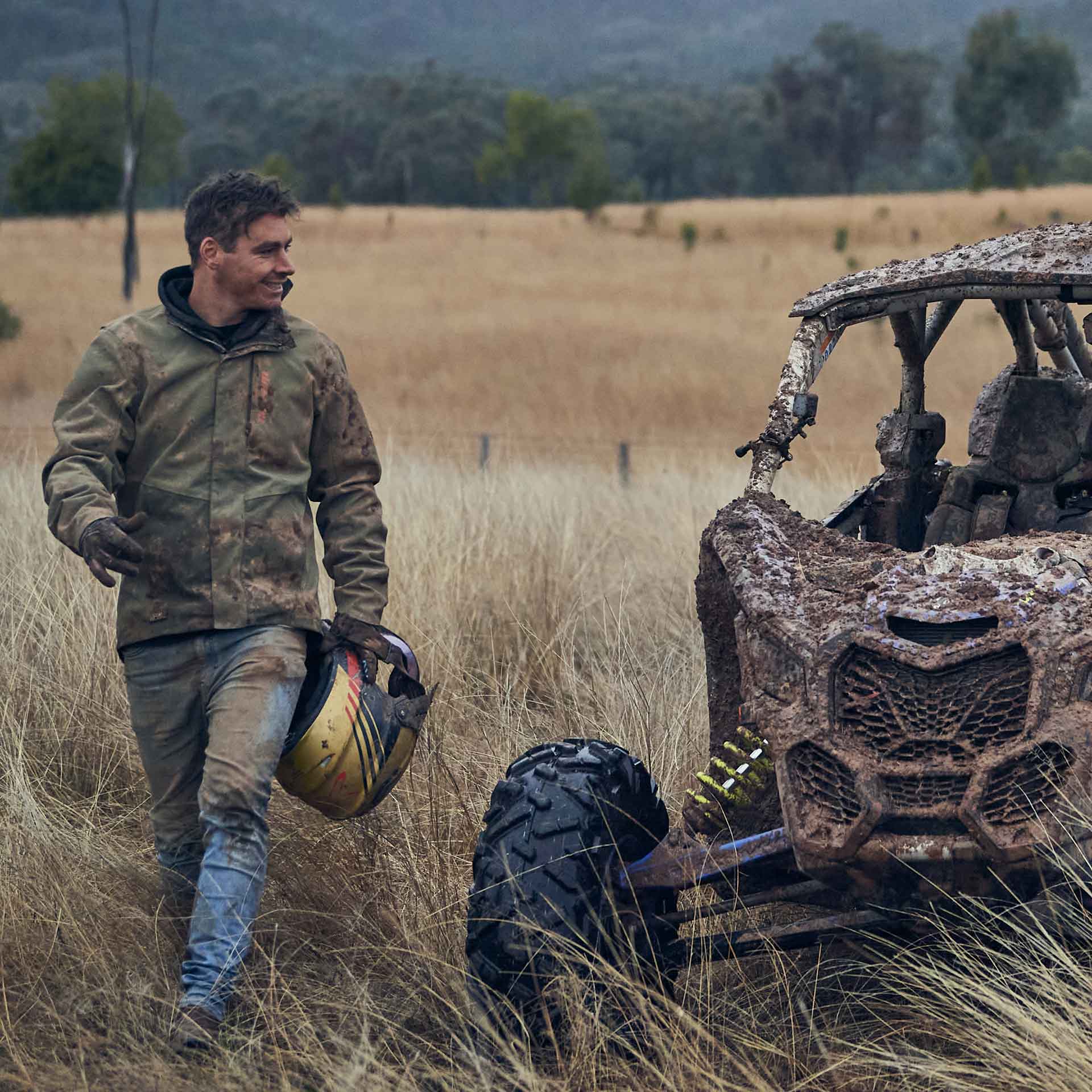 Rider walking away from a mud-caked Can-Am in a paddock