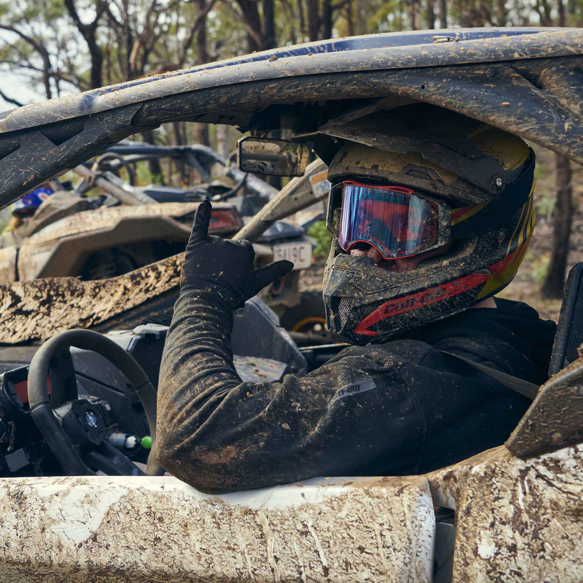 Driver giving a thumbs up from inside a mud-covered Can-Am