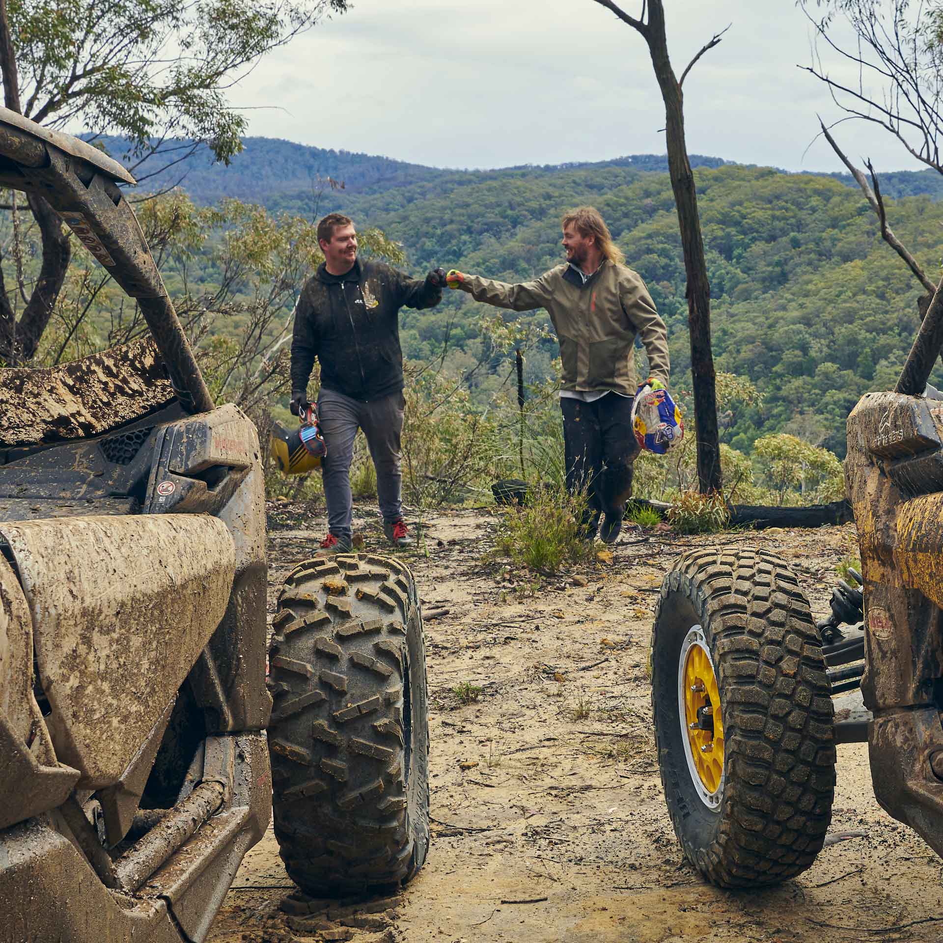 Riders taking in the view beside muddy Can-Am vehicles