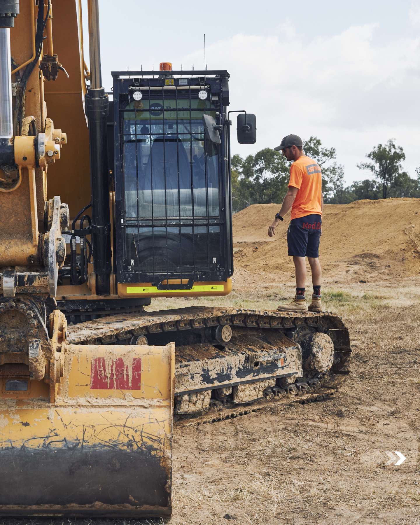 Crew member beside a Cat excavator on the build site
