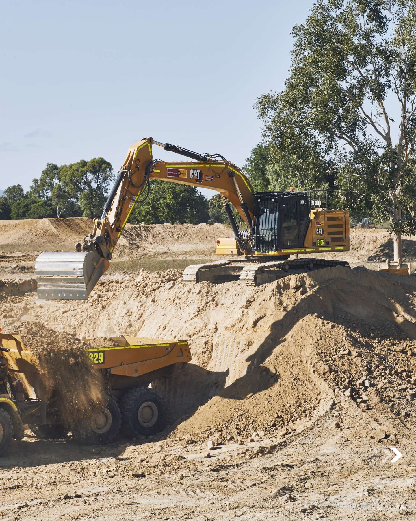 Cat excavator shaping a jump with a dump truck alongside
